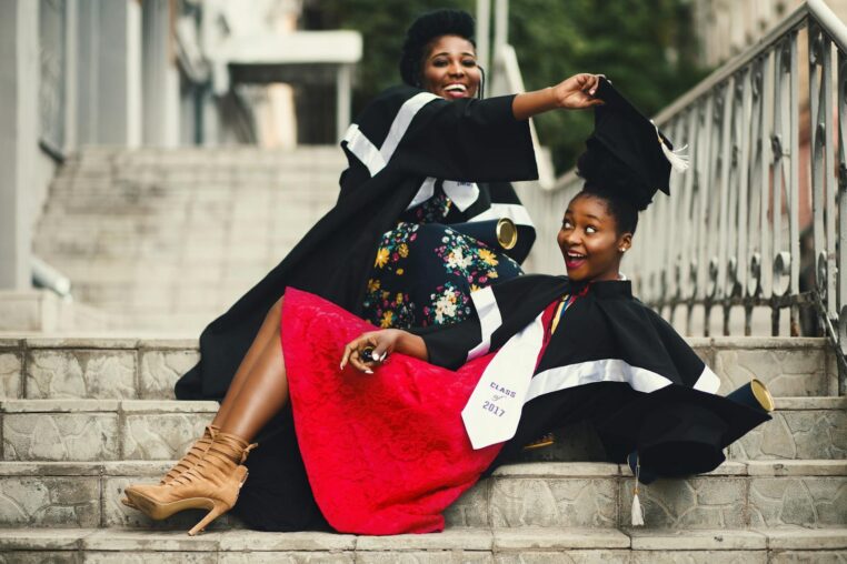 Two women in graduation gowns celebrating on stairs, embodying happiness and achievement.